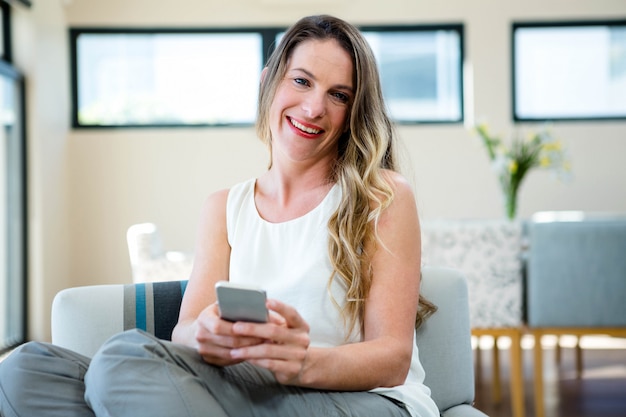 femme souriante, assise sur le canapé sur son téléphone portable