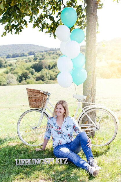 Photo une femme souriante assise contre un vélo sur le terrain pendant une journée ensoleillée