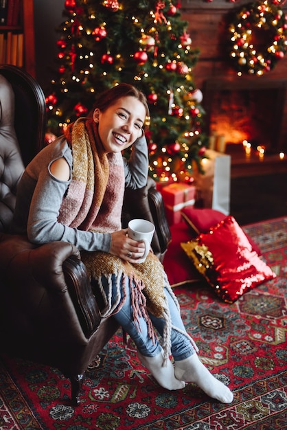 Femme souriante assise dans un fauteuil avec une tasse dans ses mains regardant la caméra et riant