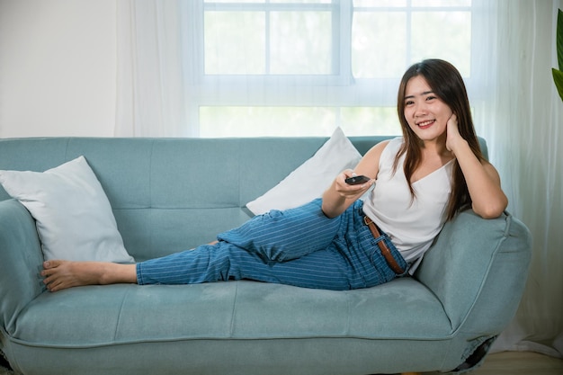 femme souriante assise à détente regardant la télévision tenant la télécommande