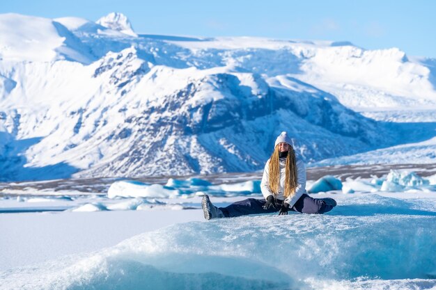 Une femme souriante assise sur la glace du lac Jokulsarlon pendant ses vacances en Islande