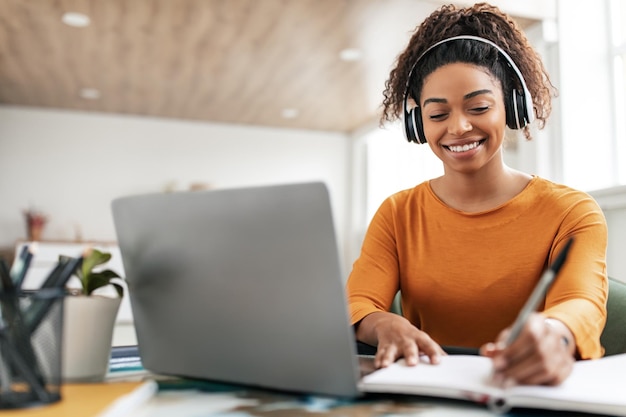 Femme souriante assise à table à l'aide d'un ordinateur écrivant dans un cahier