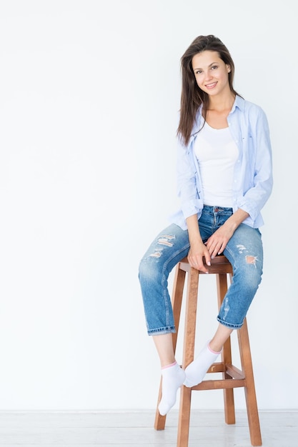 Femme souriante assise sur un tabouret en bois sur fond blanc mode de vie décontracté