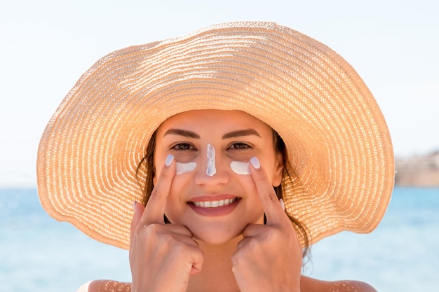 Une femme souriante au chapeau applique un écran solaire sur son visage à l'indienne