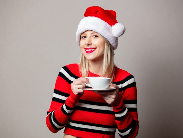 Femme souriante au chapeau de Noël avec une tasse de café sur un mur gris