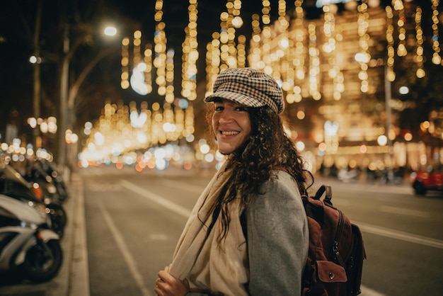 Femme souriante au milieu d'une rue décorée de lumières de Noël