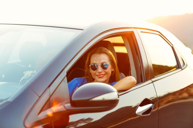 Une femme souriante au volant d'une voiture au coucher du soleil Concept de voyage