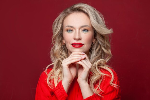 Photo une femme souriante aux cheveux blonds et aux ongles naturels sur un fond rouge vif