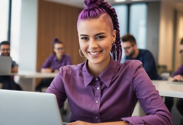 Une femme souriante aux cheveux violets travaille sur un ordinateur portable dans un bureau avec des collègues concentrés dans le