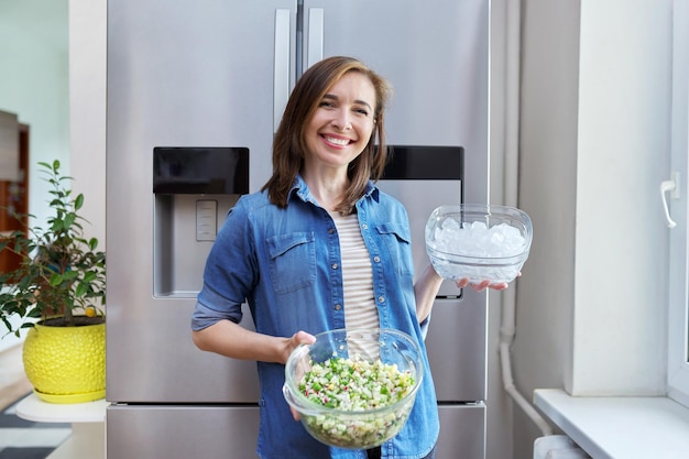 Femme souriante avec un bol de glace et une assiette de salade de légumes dans les mains