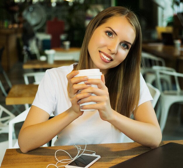 Femme souriante de bonne humeur avec une tasse de café assis dans un café