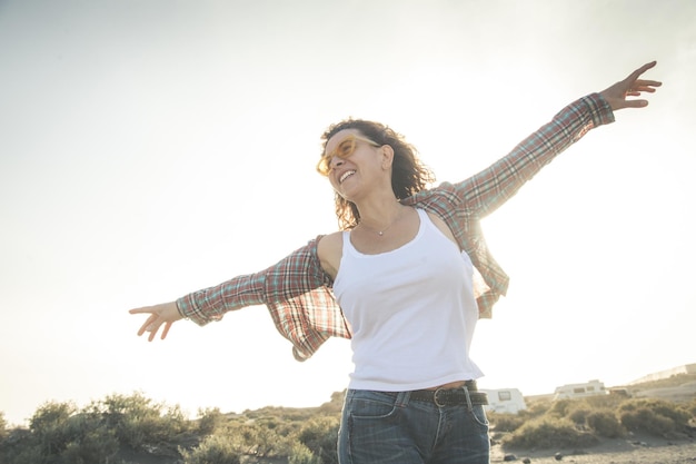 Une femme souriante avec les bras tendus debout contre un ciel clair