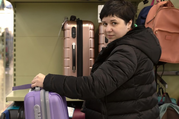 Une femme souriante choisit une grande valise de voyage pour les voyages et les loisirs Commerce de détail