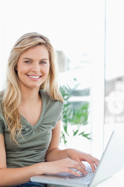 Femme souriante comme elle utilise son ordinateur portable sur le canapé, vue de côté