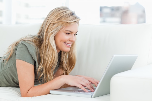 Femme souriante comme elle utilise son ordinateur portable tout en se trouvant sur le canapé