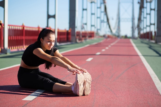 Femme souriante de coureur faisant des étirements avant de faire du jogging sur le pont. Espace pour le texte