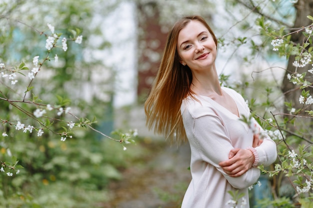 Une femme souriante dans une blouse blanche se dresse dans une fleur de cerisier