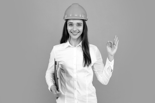 Femme souriante dans un casque de protection avec presse-papiers isolé sur fond gris