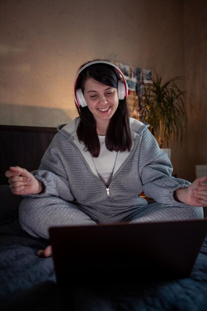 Femme souriante dans un casque travaillant sur un ordinateur portable assis sur le lit