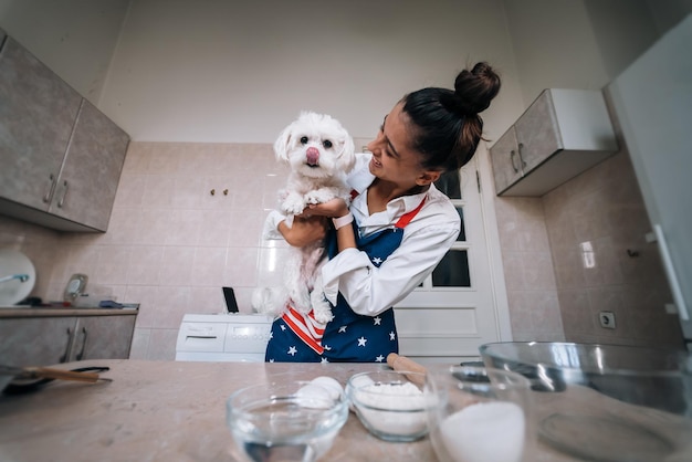 Femme souriante dans la cuisine tenant un mignon chien maltais blanc