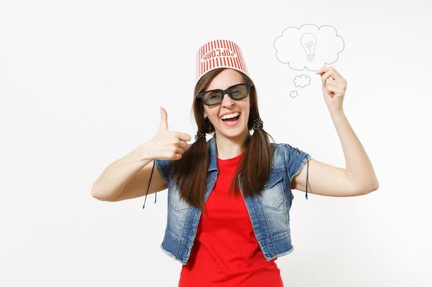 Femme souriante dans des lunettes 3d avec seau pour pop-corn sur la tête en regardant un film, tenant un nuage avec une ampoule, une idée et montrant le pouce vers le haut isolé sur fond blanc. Les émotions au cinéma.