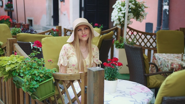 Femme souriante dans un restaurant extérieur. Gaie jeune jeune femme assise à table dans un restaurant extérieur sur une rue confortable.