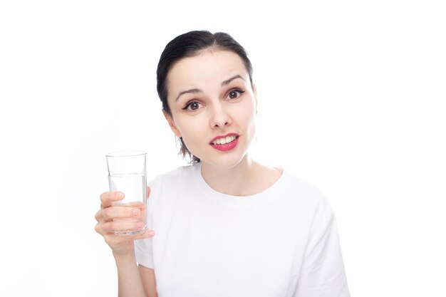 femme souriante dans un t-shirt blanc tient un verre d'eau dans sa main fond de studio blanc