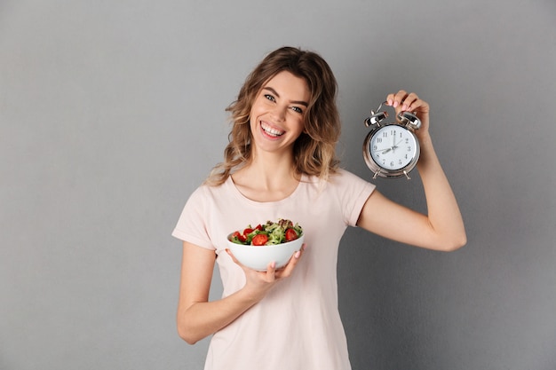 Femme souriante, dans, t-shirt, sur, régime, tenant plaque, à, légumes, et, réveil, quoique, sur, gris