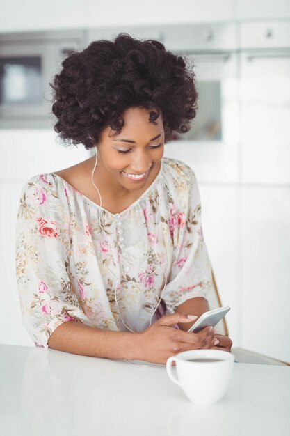 Femme souriante avec des écouteurs à l&#39;aide de smartphone dans la cuisine