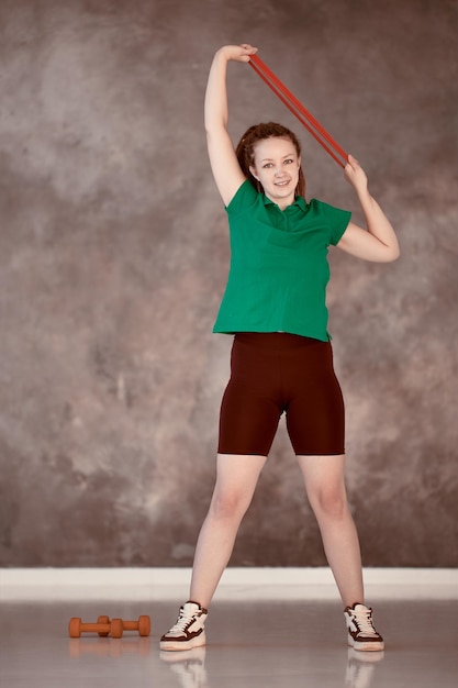 Une femme souriante étend une bande élastique sportive au-dessus de sa tête pendant l'entraînement en force au gymnase