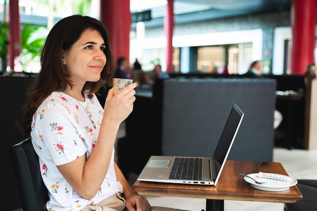 Femme souriante avec une expression positive tenant une tasse de café en regardant à distance