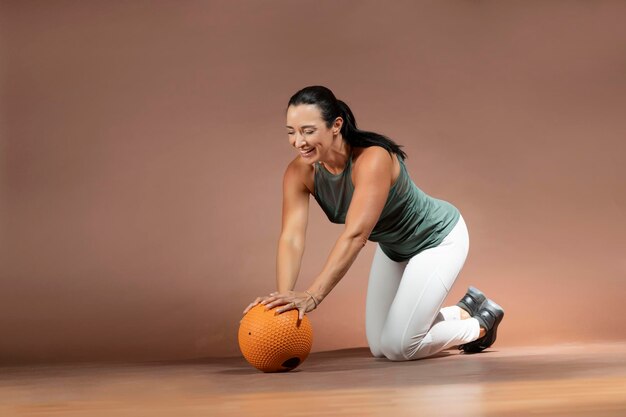 Photo femme souriante faisant de l'exercice avec une balle de médecine contre le mur