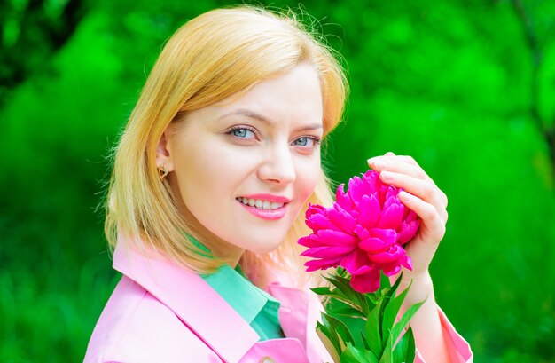 Femme souriante avec fleur rose et fond de végétation floue.