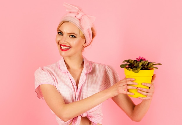 Femme souriante avec fleur de Saintpaulia en pot. Fille cultivant des fleurs. Violettes africaines de Saintpaulia.