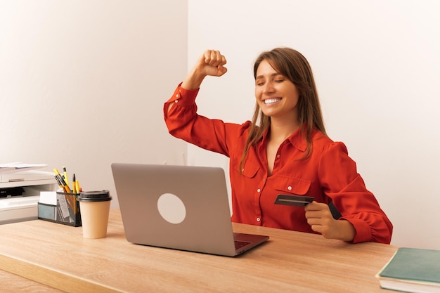 Une femme souriante a gagné un prix en tenant une carte de crédit devant son ordinateur portable