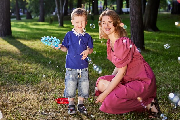 Une femme souriante et un garçon jouent avec des bulles à l'extérieur