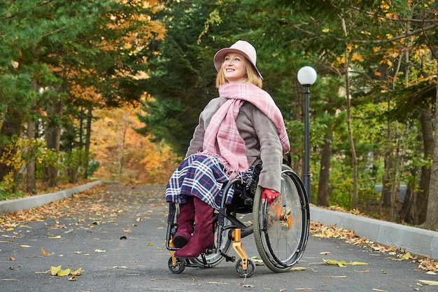 Femme souriante handicapée paralysée dans un fauteuil roulant se déplace dans le parc d'automne