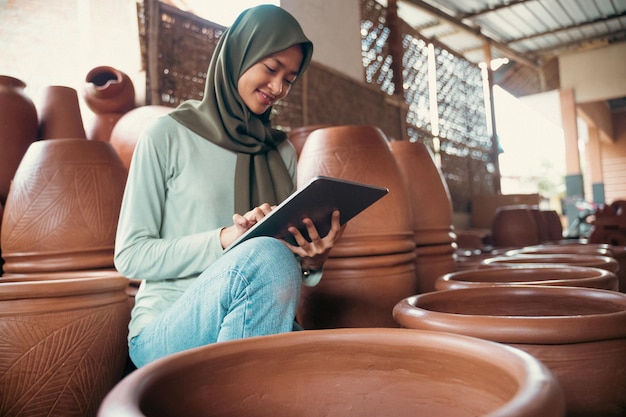 Femme souriante en hijab à l'aide d'une tablette entre poterie