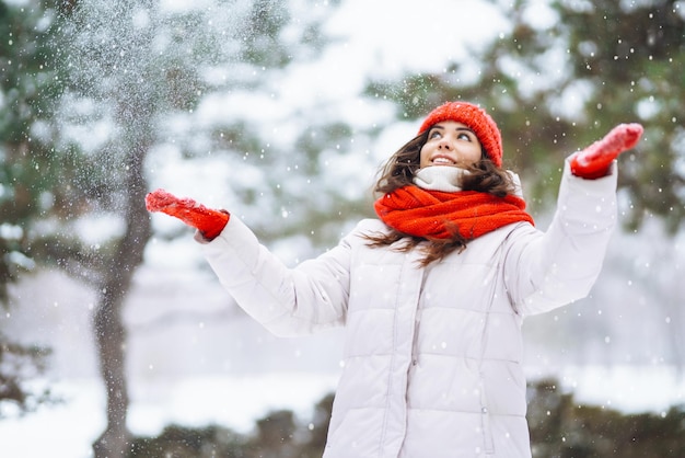 Femme souriante d'hiver au chapeau rouge posant dans un parc enneigé