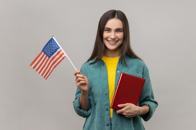 Femme souriante intelligente tenant dans les mains un livre et des cours d'éducation au drapeau américain à l'étranger