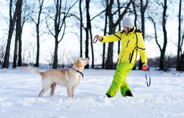 Femme souriante jouant avec mignon jeune chien retriever dans la nature d'hiver