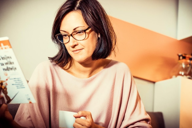 Photo une femme souriante lisant un roman tout en se relaxant à la maison et en buvant du café.