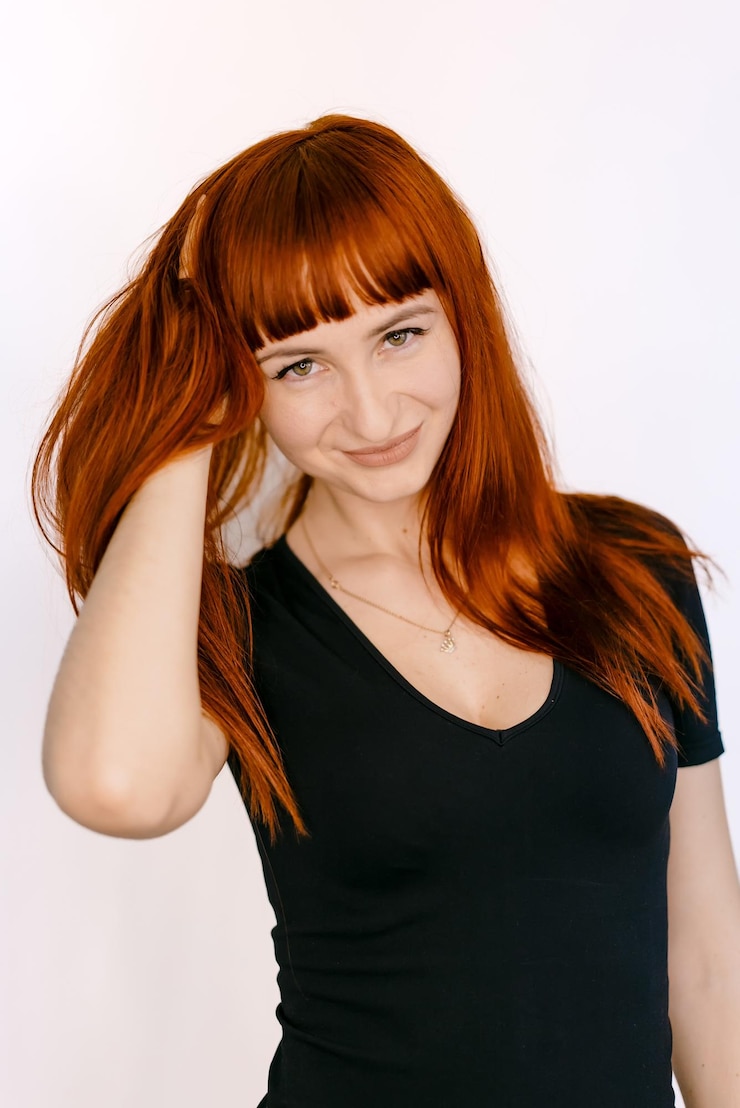 Photo une femme souriante avec de longs cheveux rouges sur un fond blanc une femme aux cheveux rouges vibrants sourit tout en touchant joueusement ses cheveux sur un fond propre