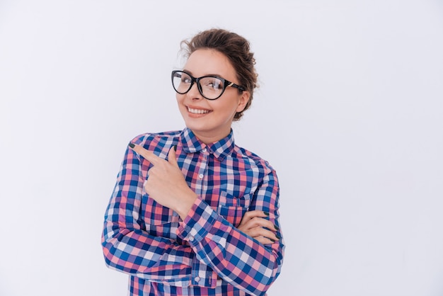 Femme souriante à lunettes et chemise à carreaux pointant vers l'extérieur