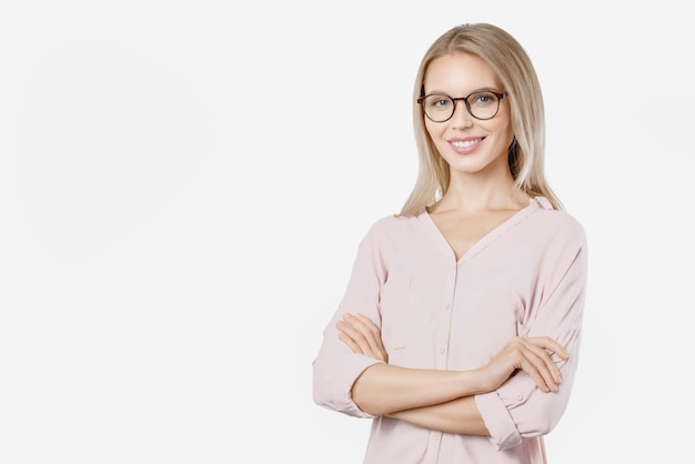 Femme souriante à lunettes posant avec les bras croisés et regardant la caméra sur fond blanc