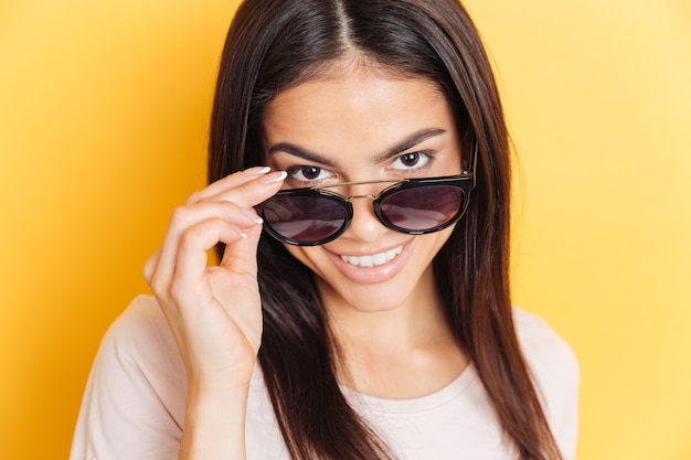 Femme souriante à lunettes de soleil regardant devant le mur jaune