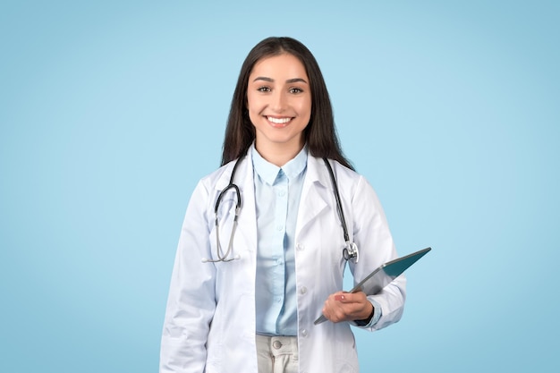 Une femme souriante, médecin, tenant un bloc-notes sur un fond bleu