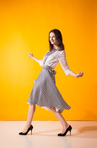 Femme souriante à la mode en belle robe posant au studio, mouvement tourné sur jaune