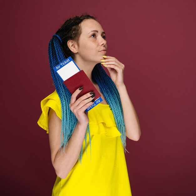 Une femme souriante à la mode moderne en robe jaune avec des billets d'avion et un passeport à la main