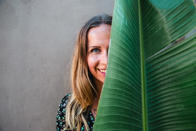 Une femme souriante avec la moitié de son visage couvert d'une photo de feuille de banane avec un espace de copie